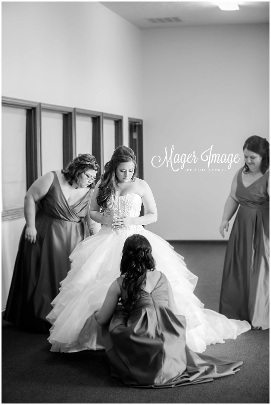 black and white photo of bride getting into her ballgown with bridesmaids help
