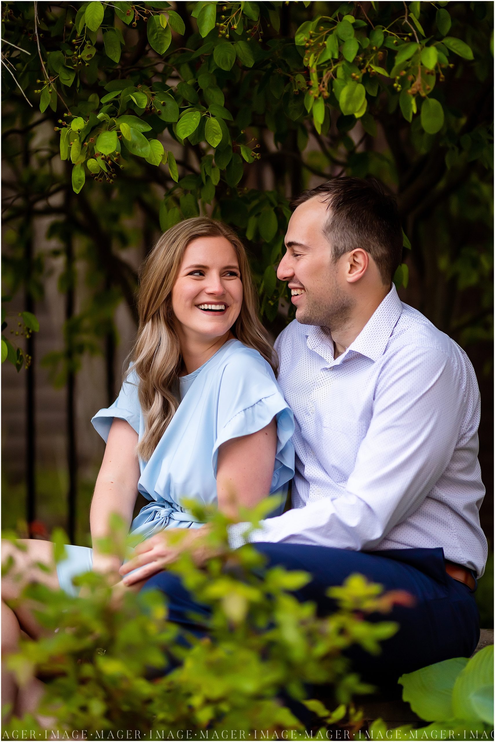 A couple sits and smiles at each other on a bench surrounded by greenery during their downtown Danville, IL engagement session.

Photo taken by Mager Image Photography 