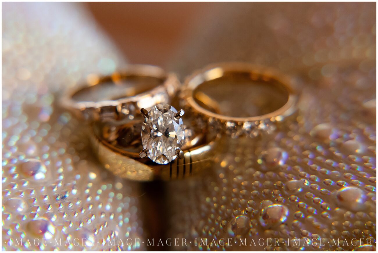 A small town wedding detail photo of the couple's rings. The bride's engagement ring and two wedding bands lay atop the groom's band. All are sitting on the bride's pearl studded shoes.

L'erable, IL. Photo taken by Mager Image Photography.