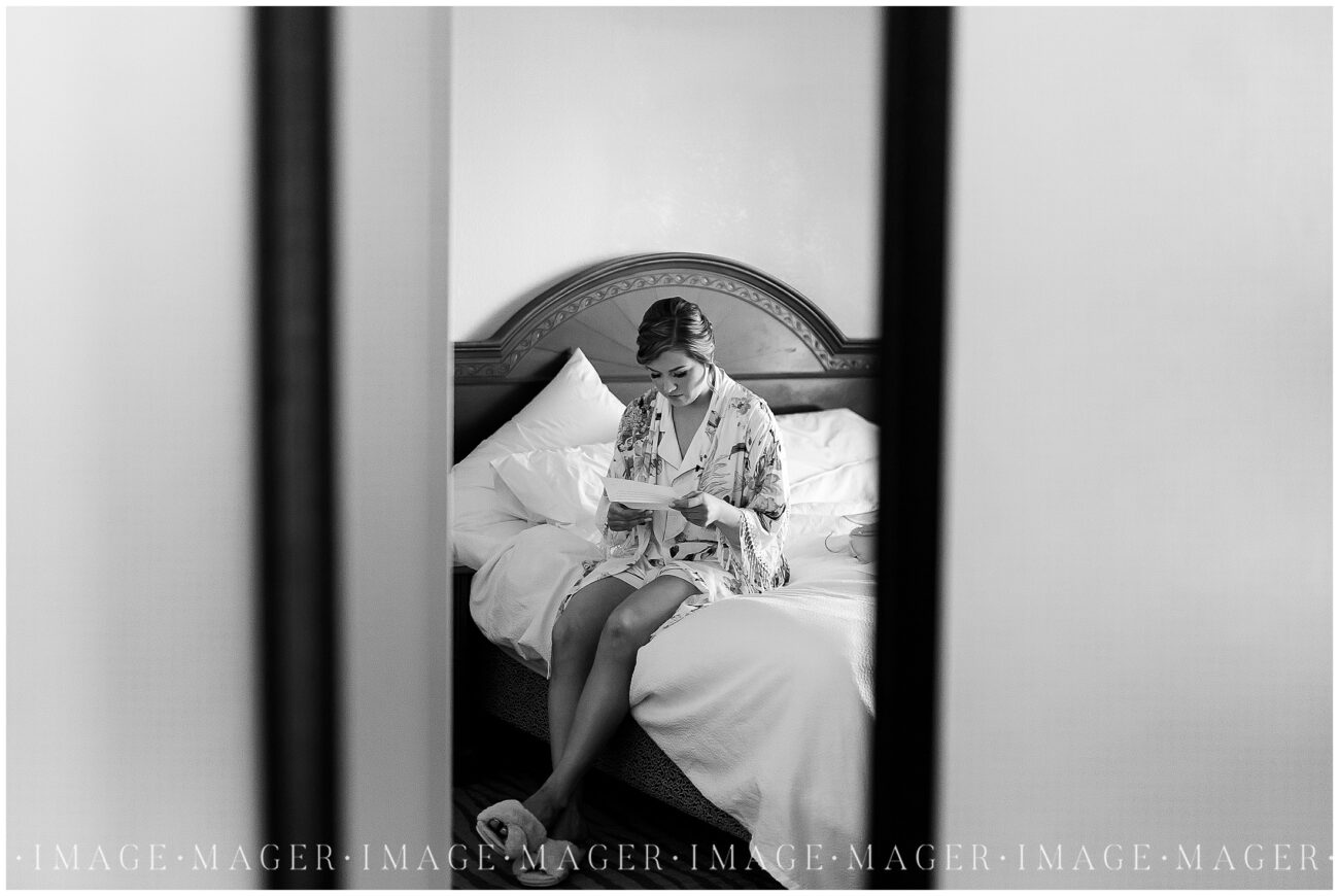 A small town wedding getting ready photo of the bride reading a note from her groom while sitting on a bed in another room.

L'erable, IL. Photo taken by Mager Image Photography.