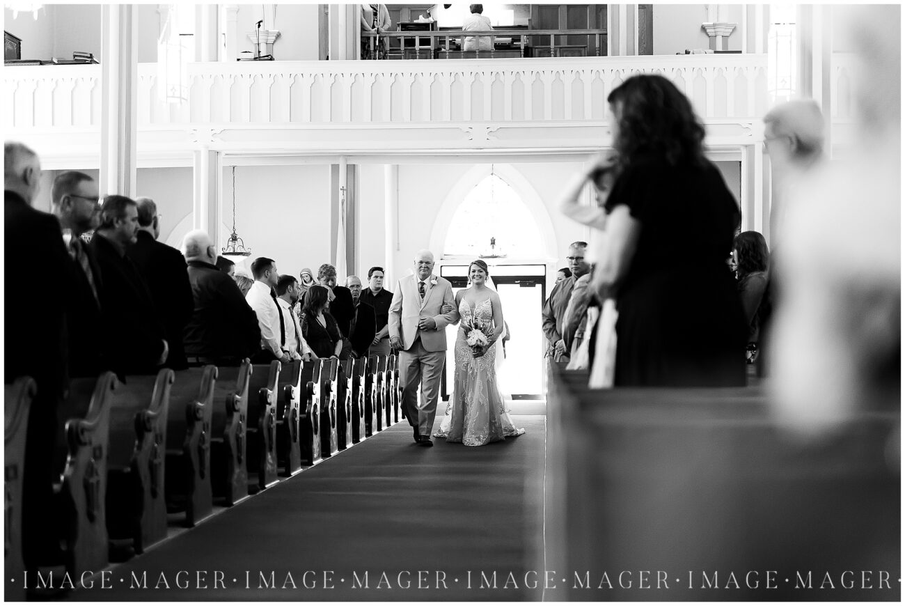A small town wedding for Casey and Adam. A black and white image of the bride walking down the aisle of the church with her dad.

Saint John the Baptist Catholic Church, L'erable, IL. 

Photo taken by Mager Image Photography.