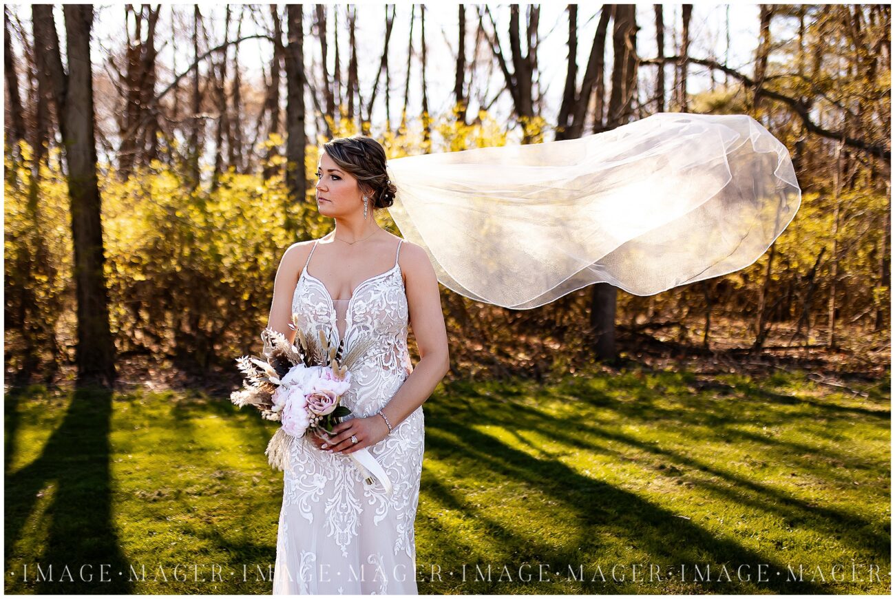 A small town wedding for Casey and Adam. The bride poses for an outdoor portrait looking away from the camera and holding her bouquet. Her long veil is flying in the wind.

Saint John the Baptist Catholic Church, L'erable, IL. 

Photo taken by Mager Image Photography.